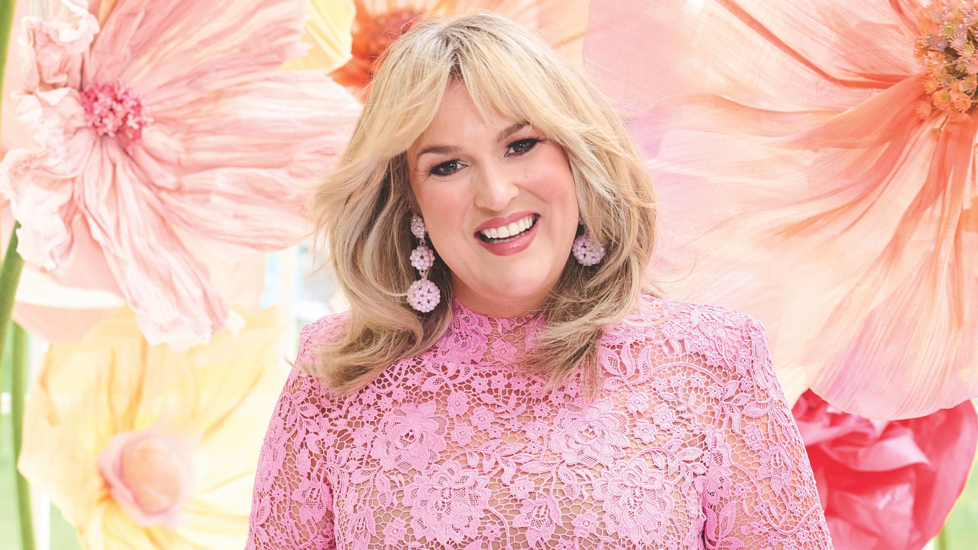 Sara Davies pictured with glowing skin in a pink lacy dress in front of a floral backdrop