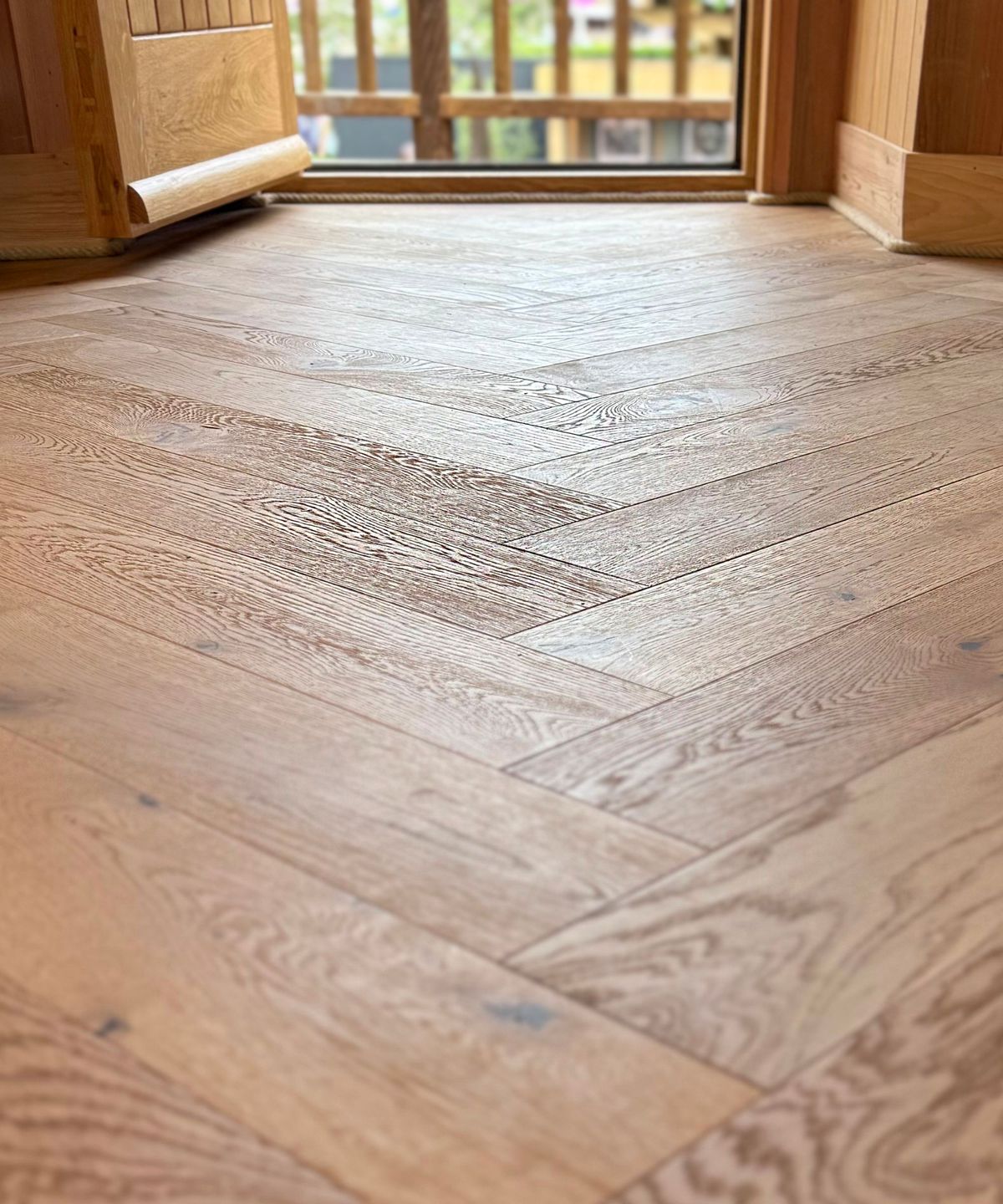 Close-up view of light oak herringbone wood flooring inside a timber-clad treehouse. The natural finish and precision laying pattern highlight quality craftsmanship and warm, modern rustic design.