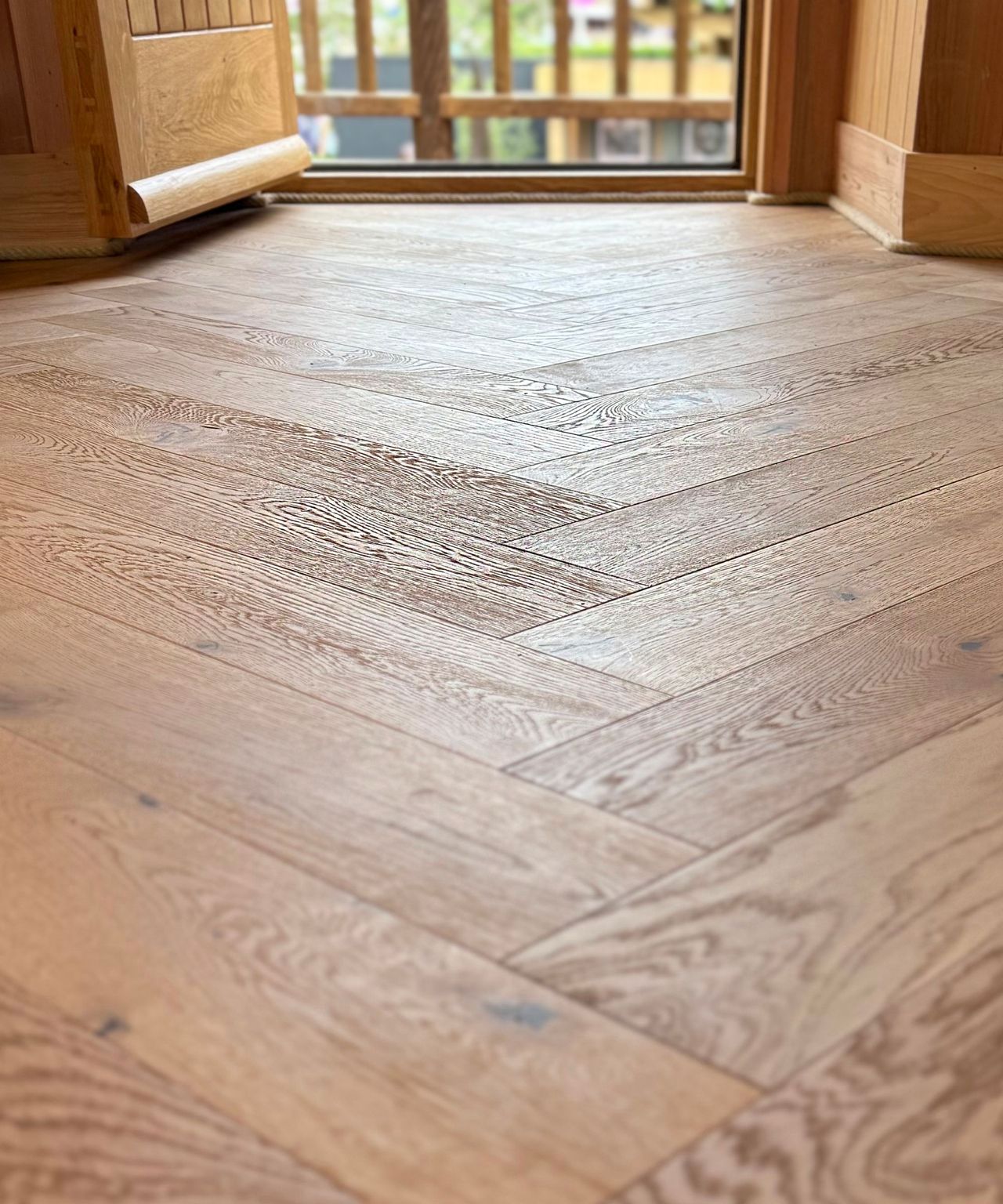 Close-up view of light oak herringbone wood flooring inside a timber-clad treehouse. The natural finish and precision laying pattern highlight quality craftsmanship and warm, modern rustic design.
