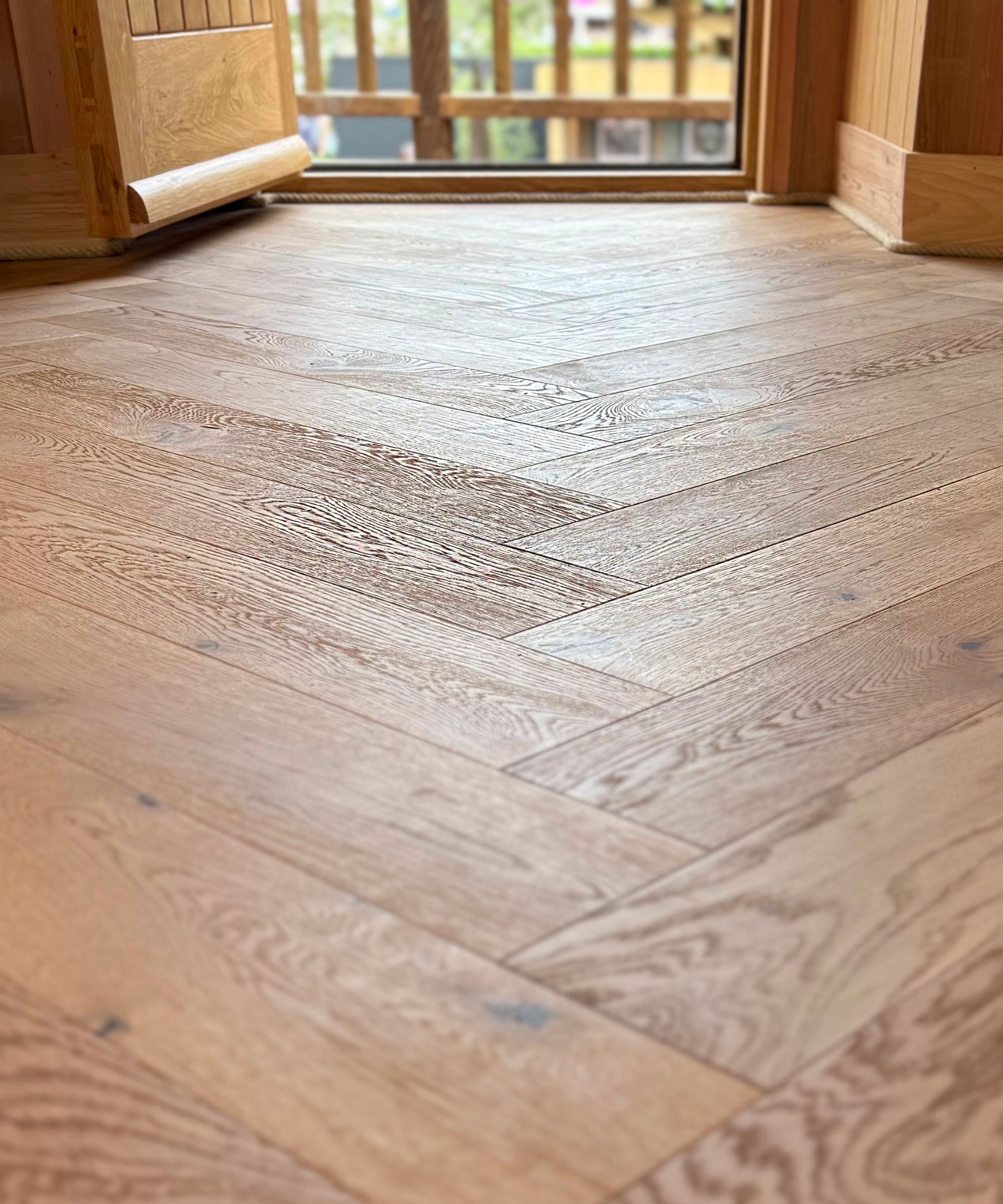 Close-up view of light oak herringbone wood flooring inside a timber-clad treehouse. The natural finish and precision laying pattern highlight quality craftsmanship and warm, modern rustic design.