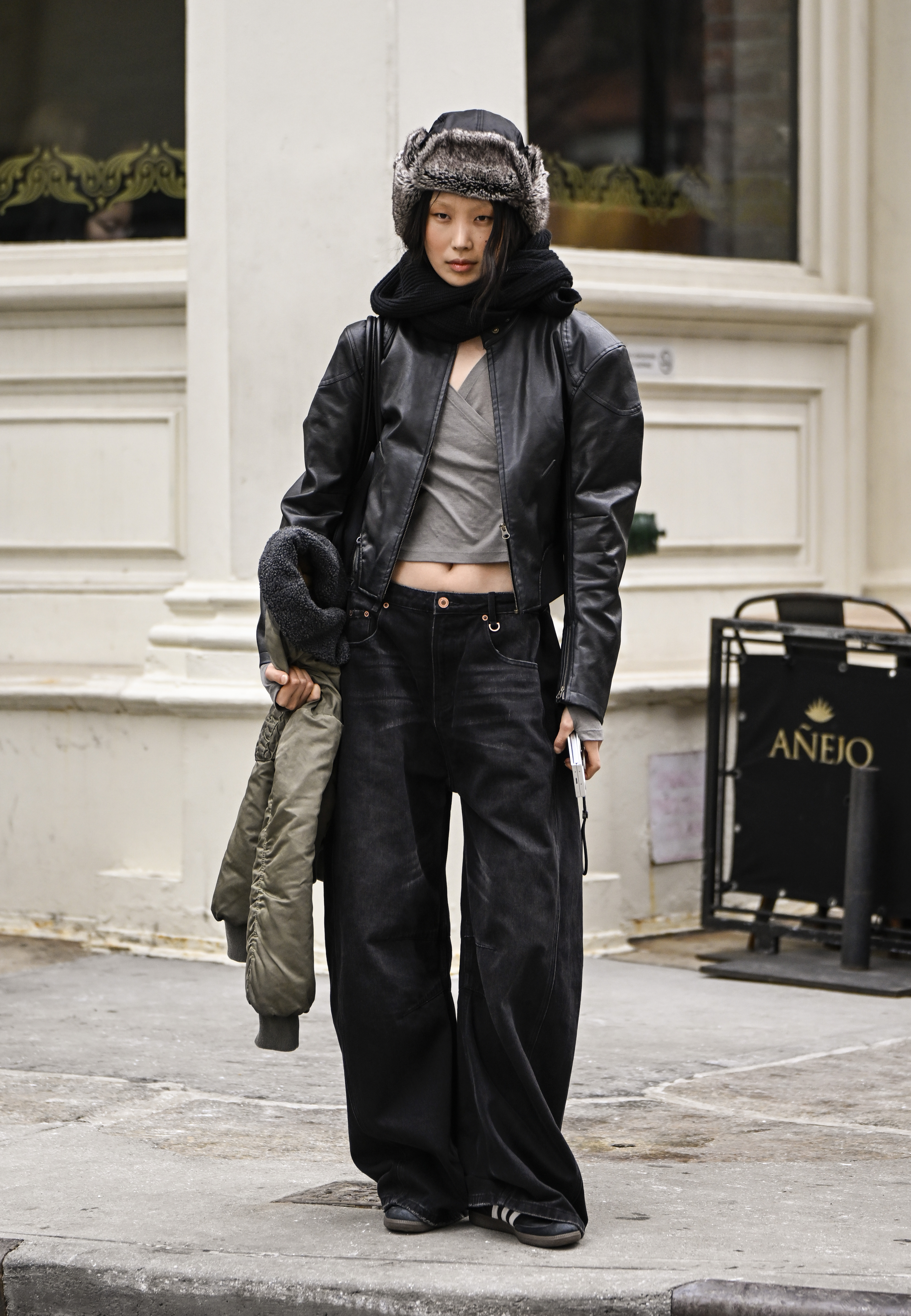 A woman wearing a leather jacket, wrap top, slouchy black jeans, and a trapper hat in street style