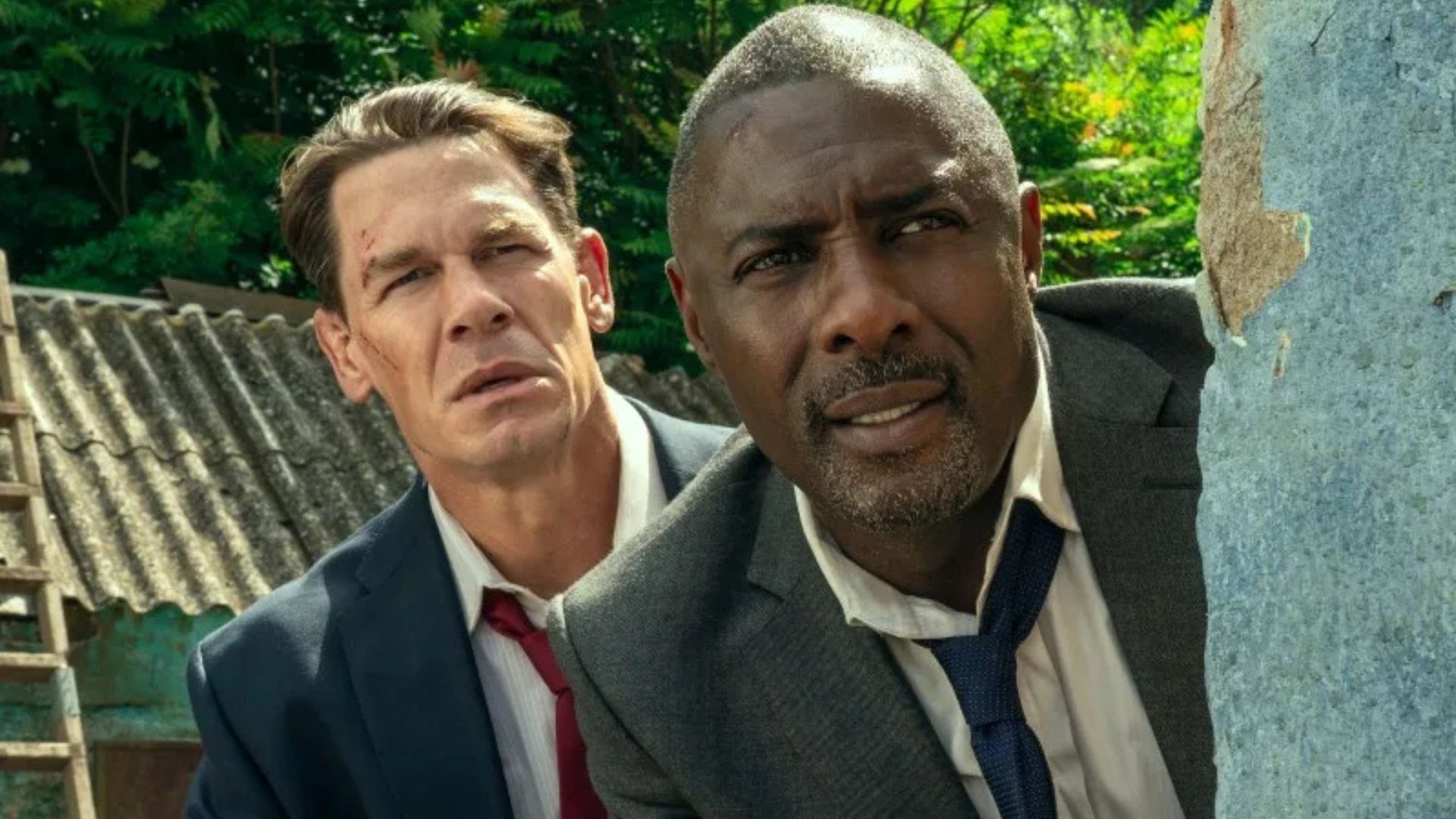 John Cena stands behind Idris Elda as they peer around a wall