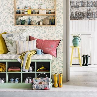 A padded storage bench with cushions against a wall with flowery wallpaper