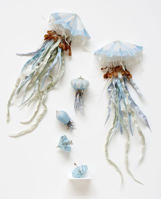 Two paper jellyfish and one small jellyfish evolving from a miniature parasol. In colours of white, light blue and brown.