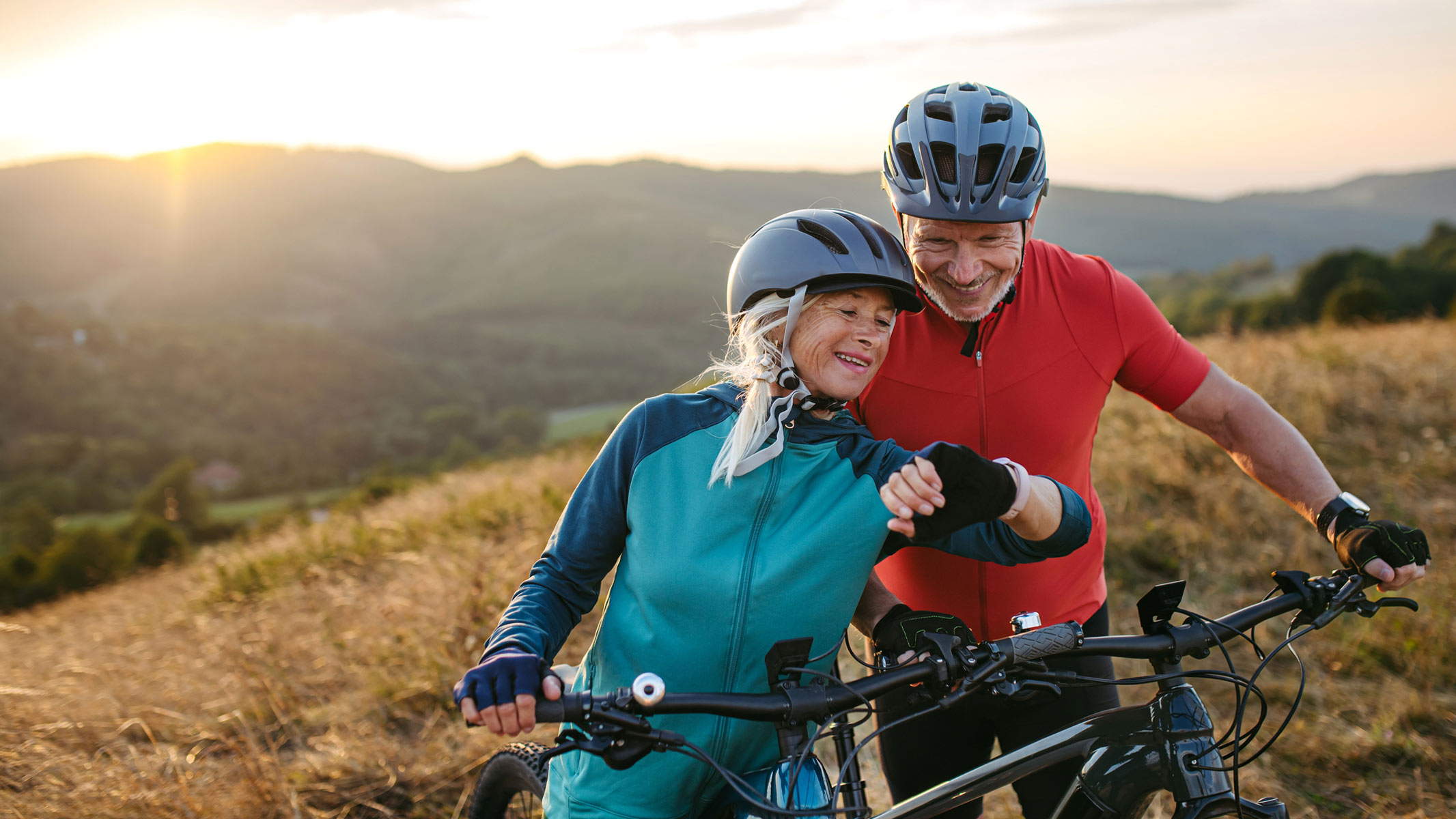 A picture of a woman showing a fitness watch to her workout partner while they are both cycling outdoors