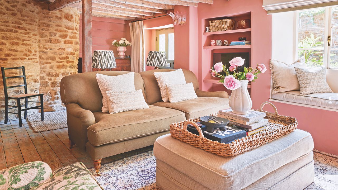 living room in small Cotswold cottage with pink painted walls, upholstered footstool and olive green sofa