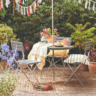 A garden with a furniture set surrounded by flower pots and a green bush with bunting hung above