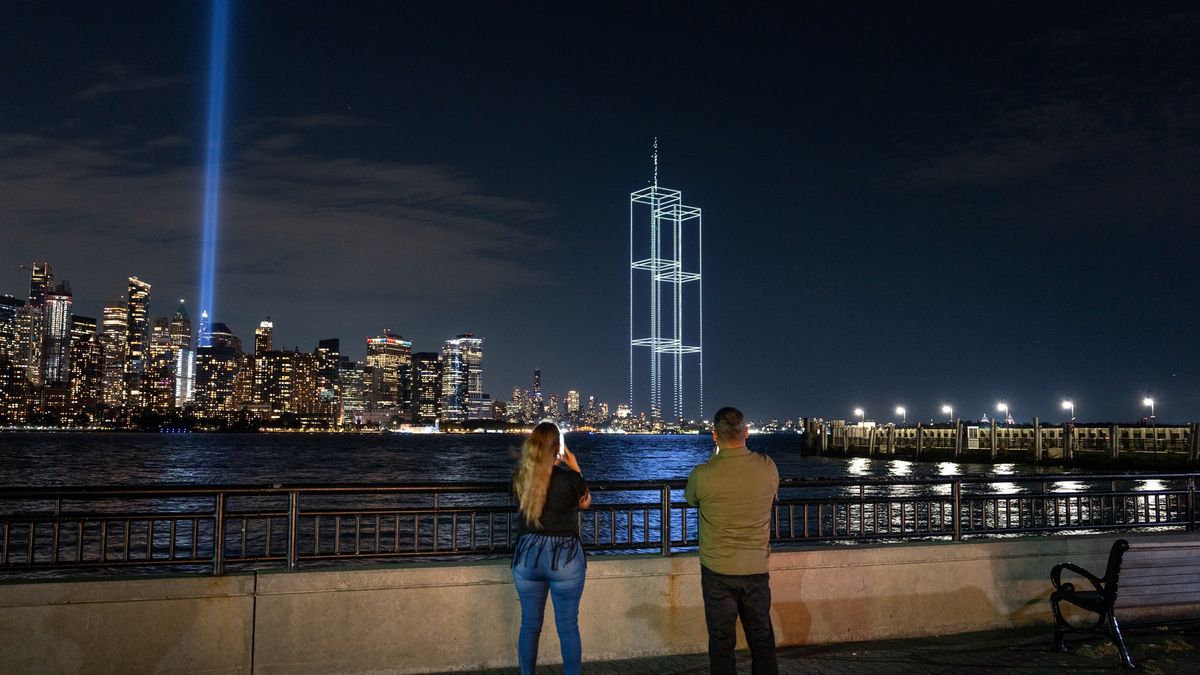 People watch and take pictures as a drone light show depicting the twin towers appears in the skyline during testing of Tribute in Light installation in lower M