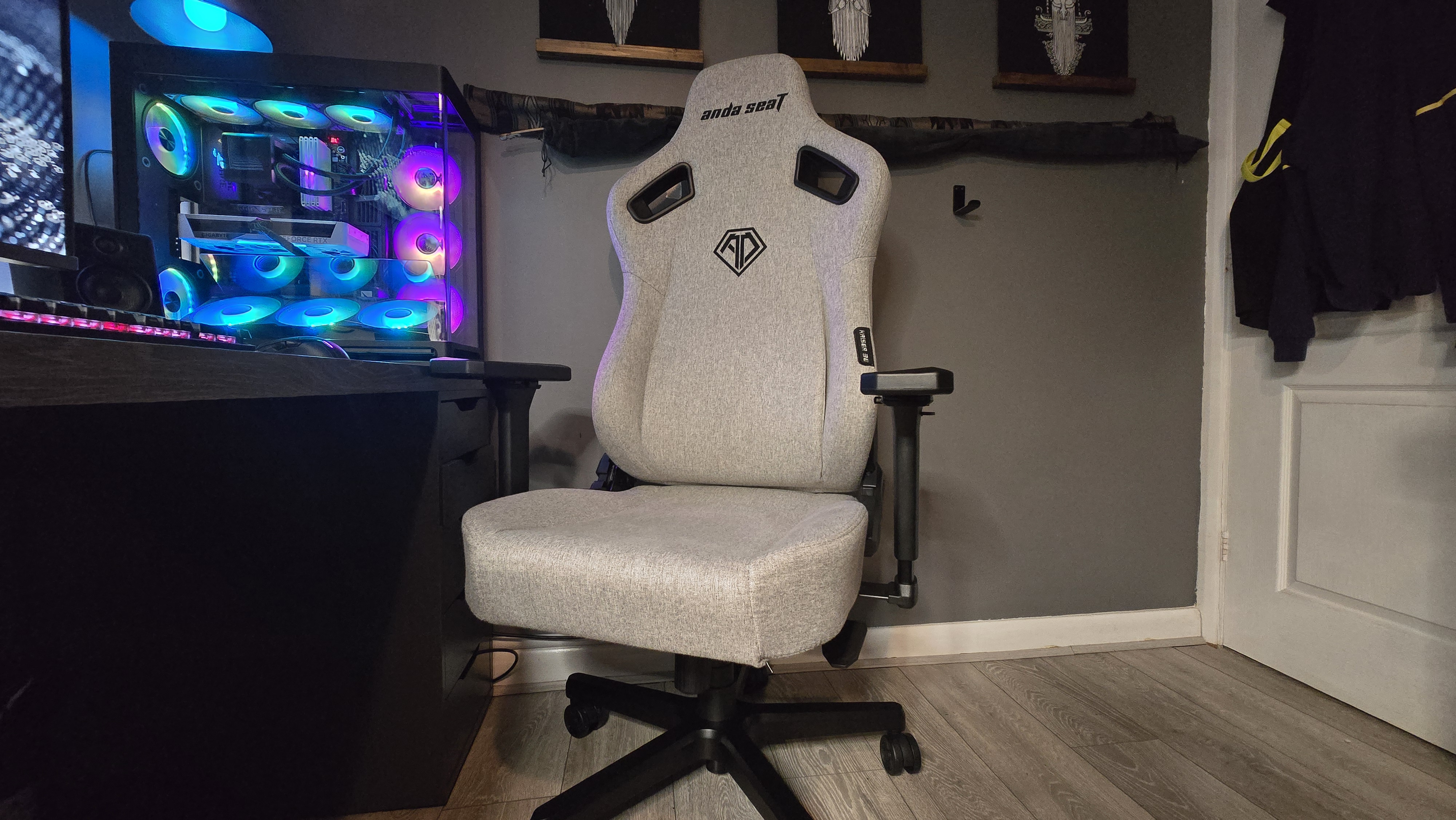 A grey gaming chair beside an RGB lighting gaming PC, desk and in an office background