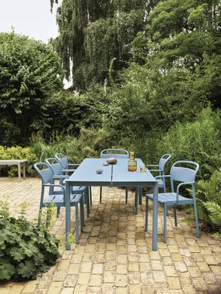 A backyard with brick flooring and a blue steel table and chairs