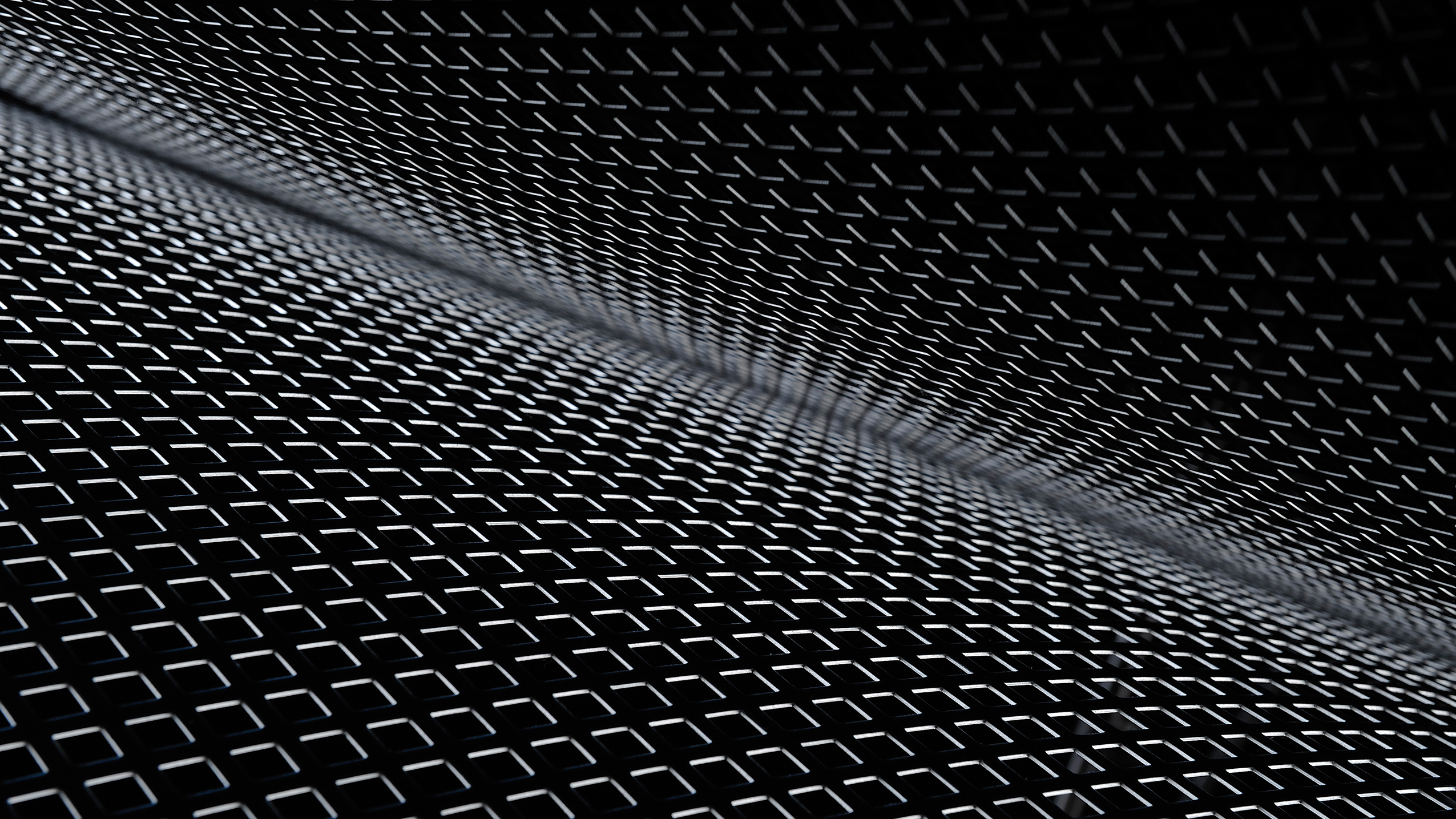 Close-up of black perforated metal sheets with diamond-shaped holes arranged in a wave-like pattern