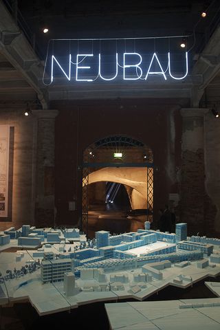 Architectural model lit in blue, under a blue neon sign reading "NAUBAU"