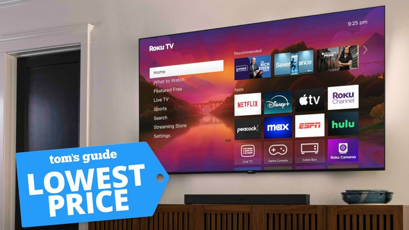 The 2025 Roku Pro Series Mini-LED TV displaying the Roku OS home screen while mounted on a living room wall. In the bottom, left-hand corner is a blue price tag that reads: &quot;Tom&#039;s Guide Lowest Price&quot;.