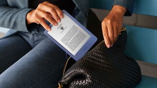 En kvinna som håller på att lägga ned en blå Amazon Kindle (2022) i sin handväska.