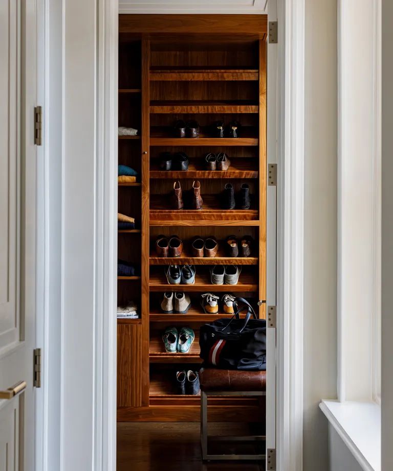 A bedroom with an open walnut closet with shoe shelves