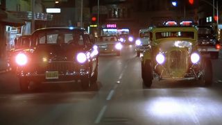 Two hot rods drive down a small town street in American Graffiti