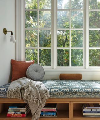 A seating nook in a window with wooden open shelves underneath and a patterned seating cushion