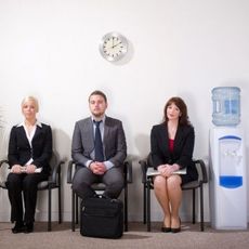 Two women and a man in business attire sitting next to a water cooler.