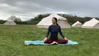 Woman sitting on yoga mat with glamping tents in the background