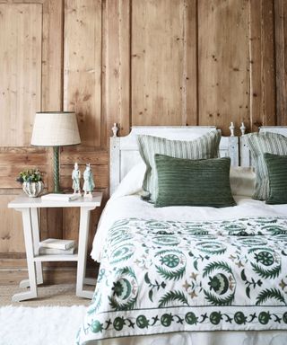 Bedroom with rustic wooden walls and bed with decorative green bedspread