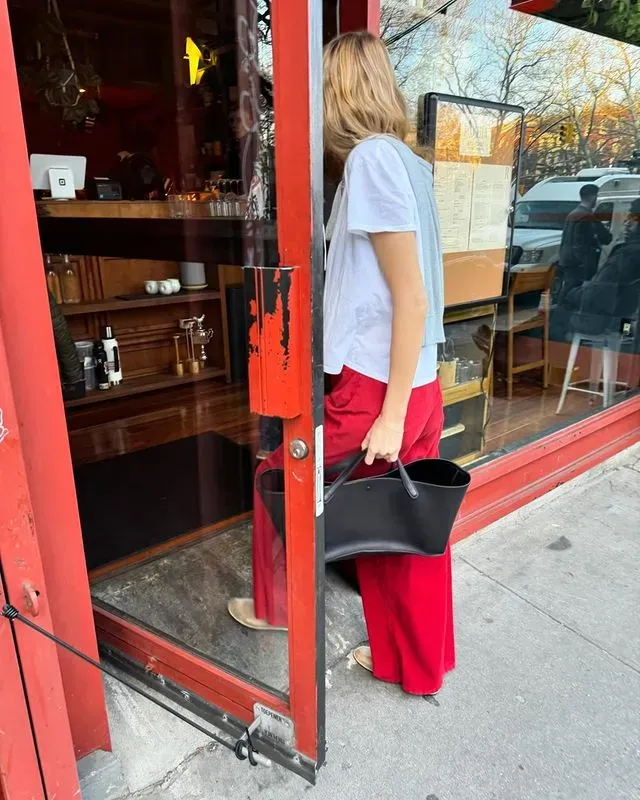 Courtney wears a white t-shirt, a black bag and red jeans.