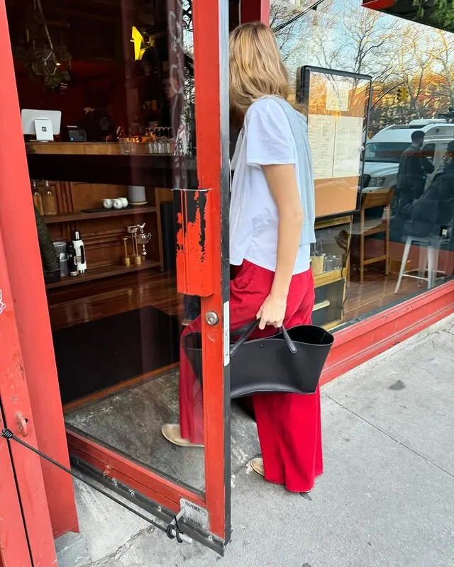 Courtney wears a white t-shirt, a black bag and red jeans.