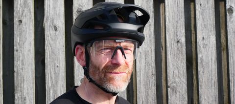 A man squinting into the sun while wearing a pair of Scott Sport Shield sunglasses and a helmet