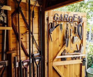 An attractive wooden garden shed with tools hanging on the wall and door