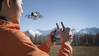 DJI Flip drone in flight, snowy mountain backdrop, person piloting using the RC2 controller in foreground