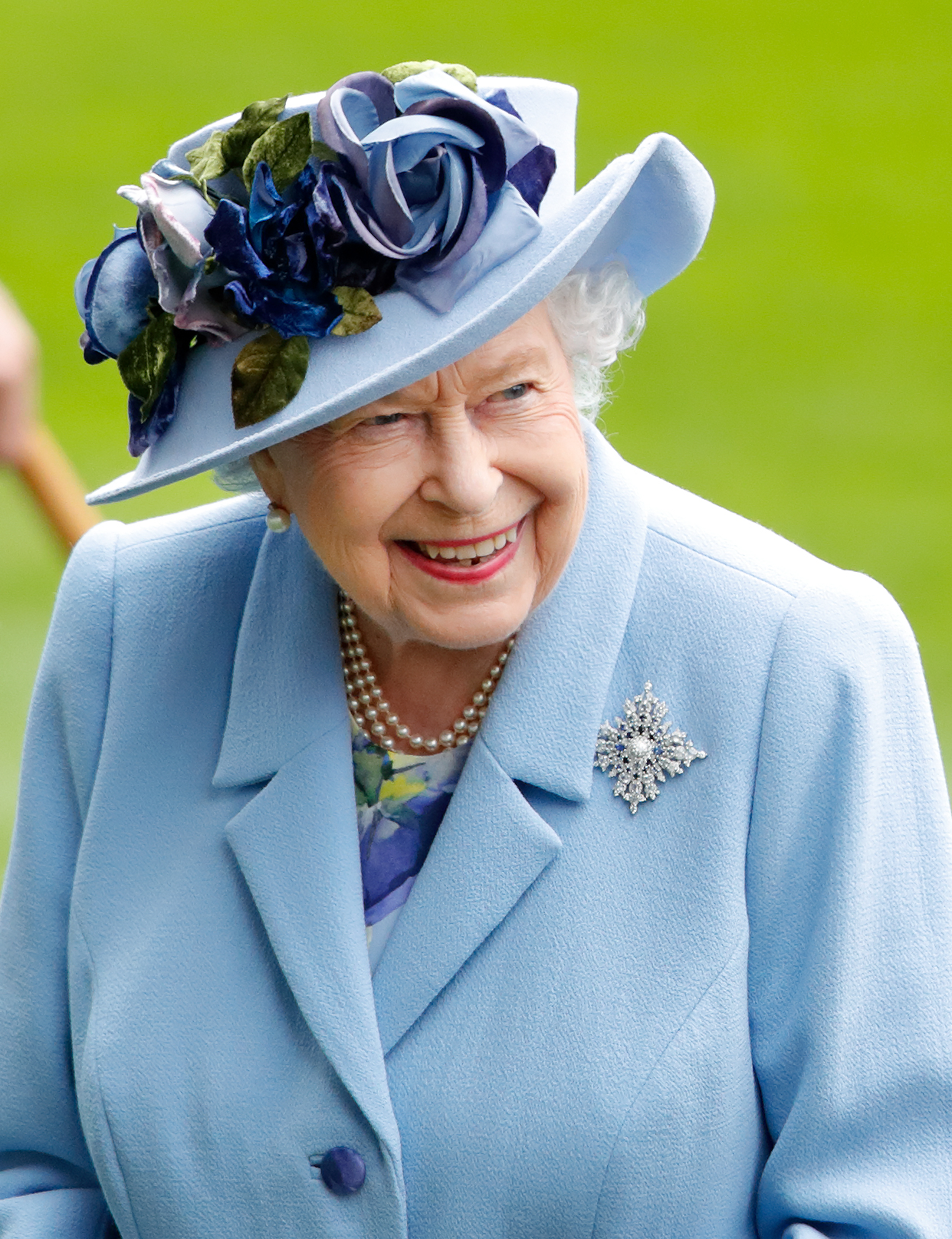 Queen Elizabeth in a blue coat and blue hat with roses on it