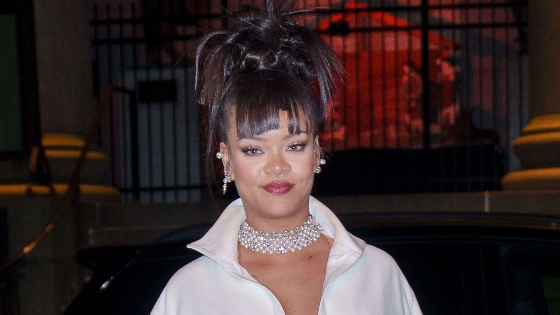 Rihanna wearing a white shirty, diamond chocker, and an updo hairstyle.