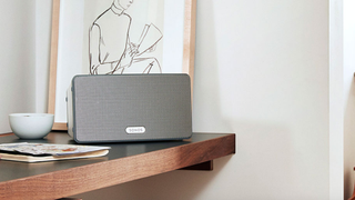 En grå Sonos Play3 står på ett skrivbord framför en enkel tavla i ett ljust rum.