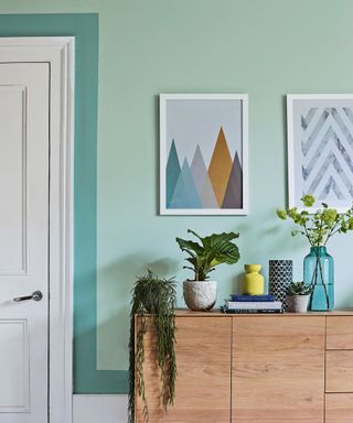 Living room with black painted floor, mint green walls and wooden sideboard.