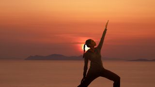 8 benefits of yoga: Woman practicing yoga at sunset near the sea