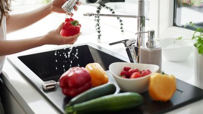 person washing peppers and other vegetables in the tap of their stainless steel sink