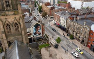 A view from a drone over a church of the painting of a woman holding a lamb on the side of a tall building