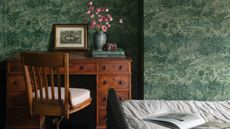 vintage style bedroom with green leafy wallpaper, a wrought iron bed and a large antique wooden desk and chair