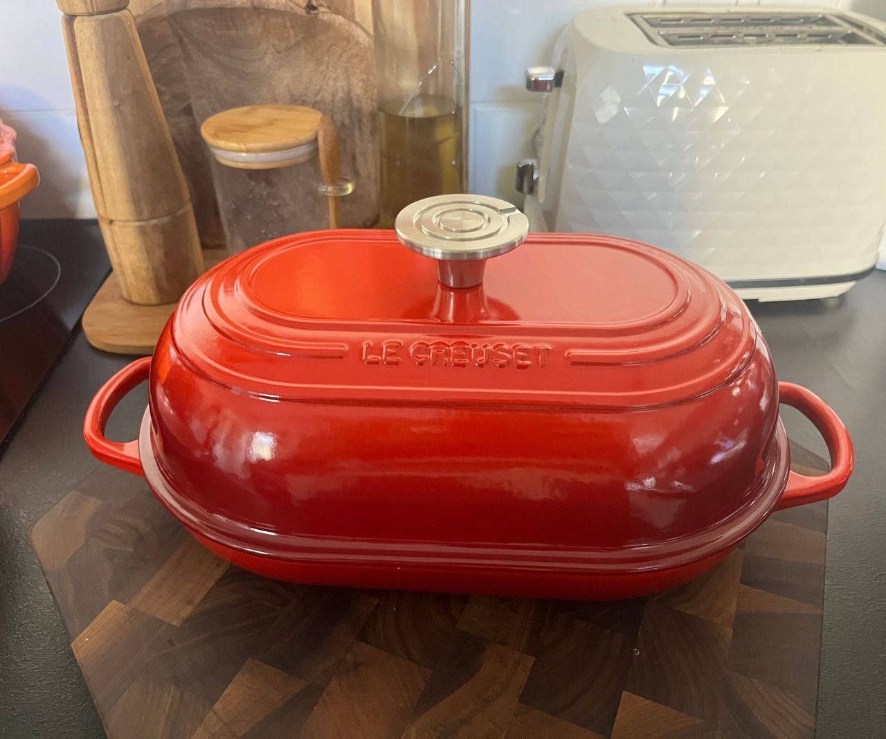 A red Le Creuset domed oval bread oven on a wooden cutting board.