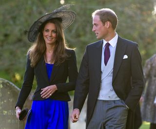 Kate Middleton wears a royal blue dress and a big black hat and black blazer to attend a wedding with Prince William