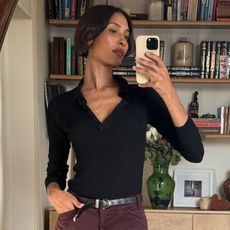a woman wearing a black polo and burgundy jeans
