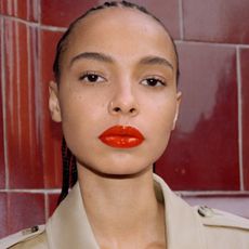 a model wears a full face of Burberry Beauty products in front of a tile wall