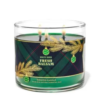 A green candle with a green tartan design with gold pine leaves