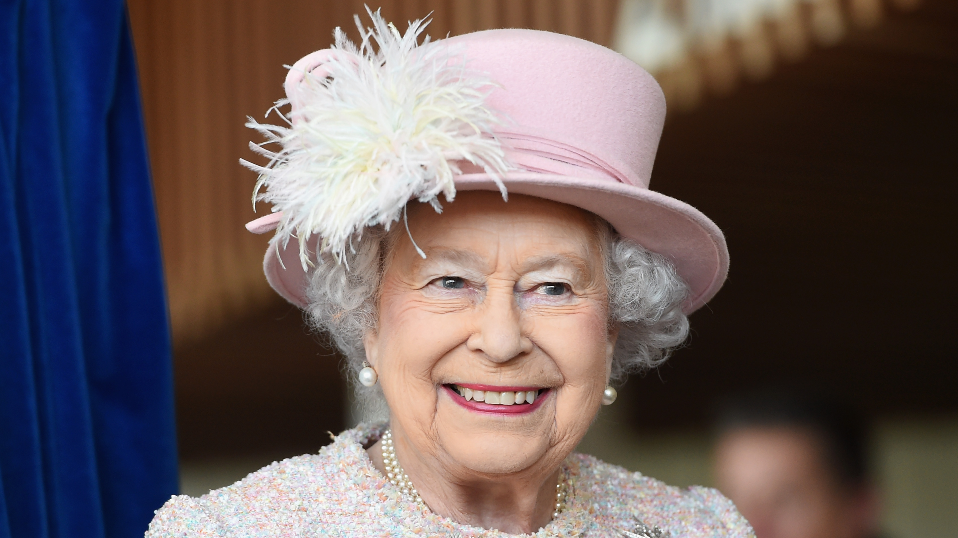 Queen Elizabeth wearing a pink hat and coat smiling