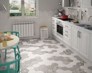a hexagonal tiled kitchen floor in grey in a white kitchen with shaker cabinets, a round dining table and blue chairs