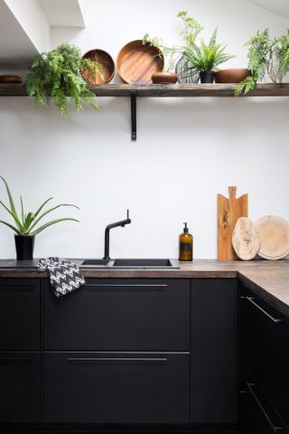 Black matt kitchen interior with wooden surfaces and houseplants on the shelf