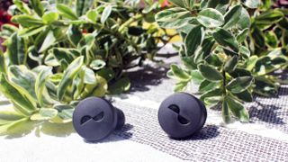 the nuratrue earbuds on an outdoor table with plants in the background