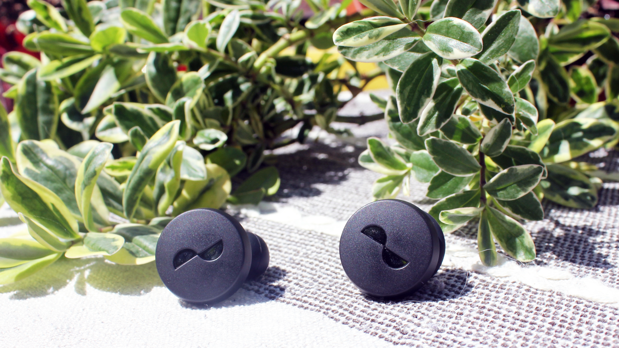 the nuratrue earbuds on an outdoor table with plants in the background