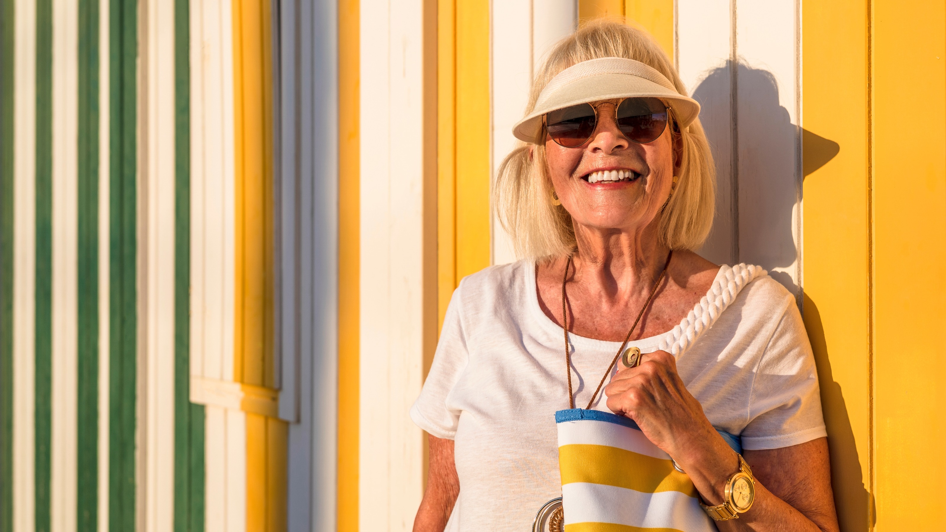 Senior woman with eyeshield and sunglasses standing in front of colorful striped wall