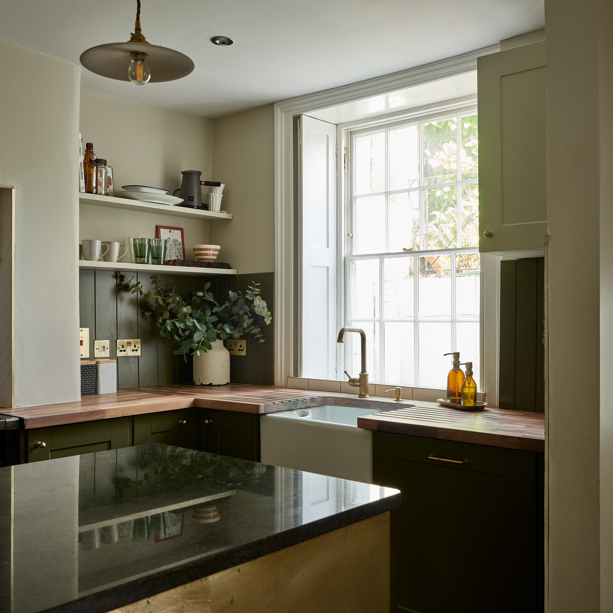 a green a white kitchen with a Belfast sink wood worktops and a large sash window