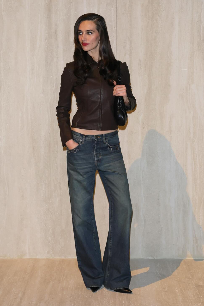 a woman wearing a cropped brown leather jacket, blue indigo denim jeans, and black pointed-toe boots
